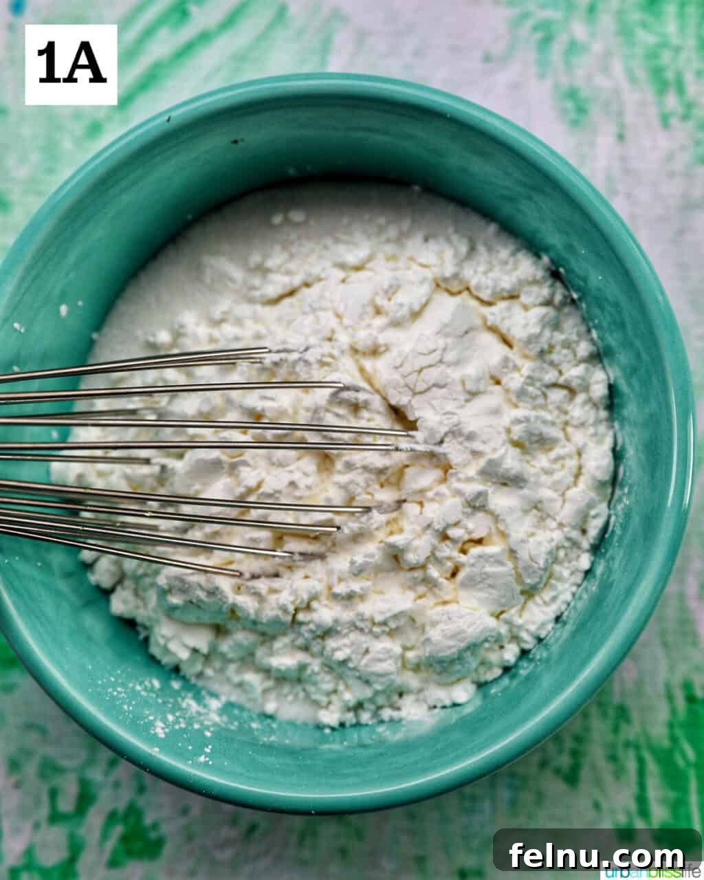 A bowl with a whisk and powdered ingredients for homemade vanilla pudding.