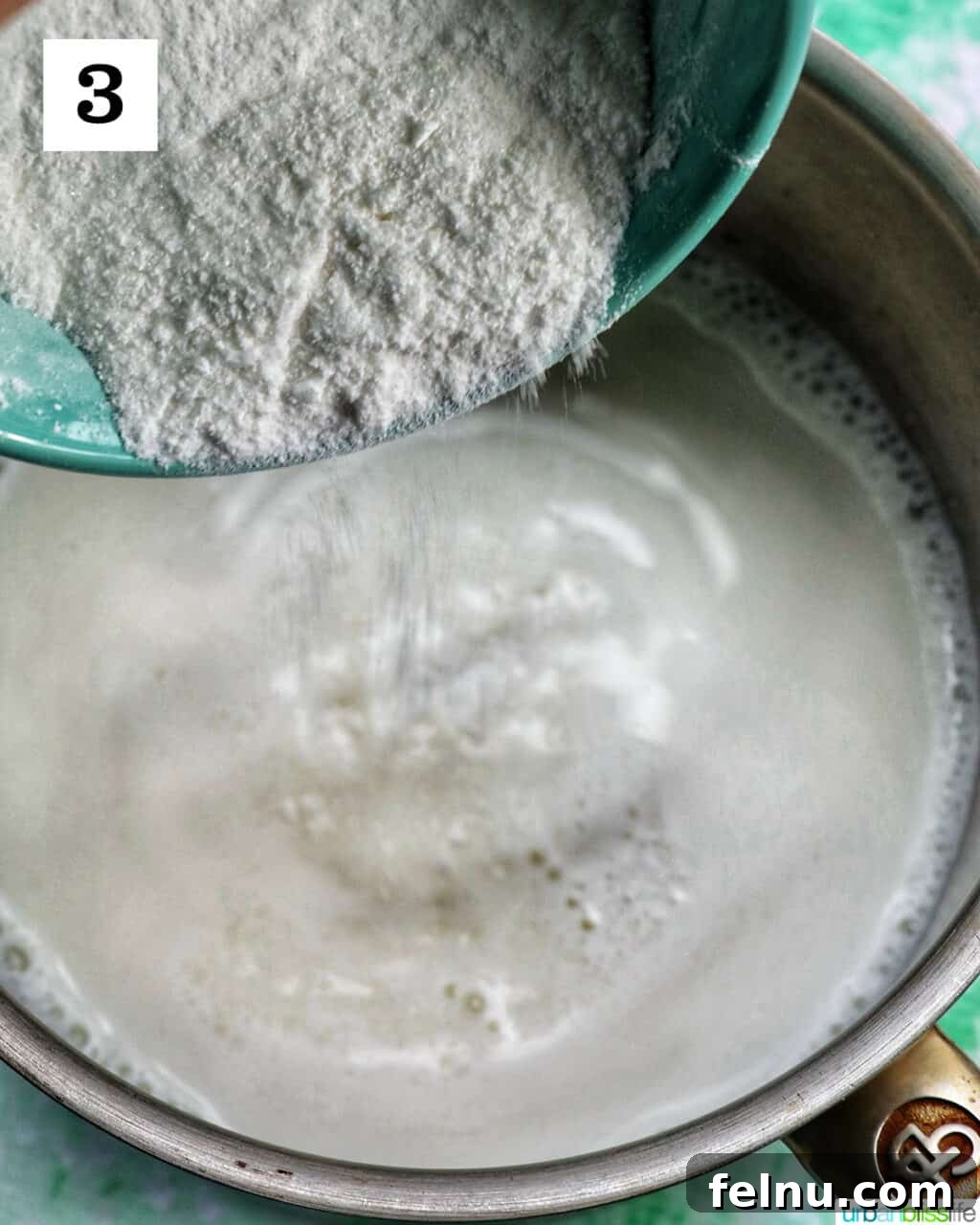 White powdered ingredients being carefully added to the warm milk in a saucepan.