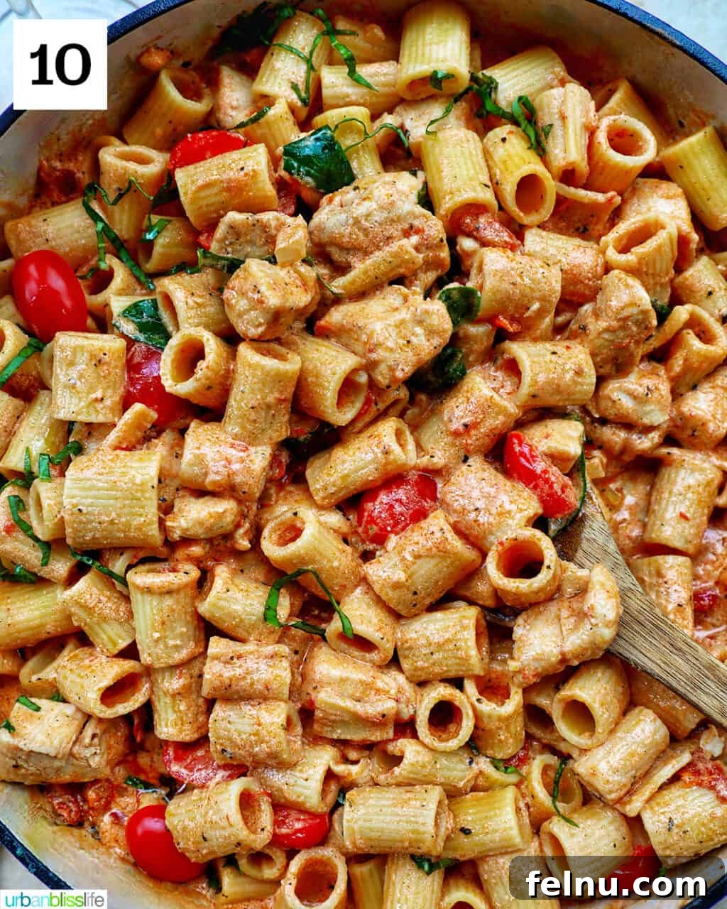 Velvety Tuscan Chicken Pasta 16 A wooden spoon stirring rigatoni pasta, chicken, and creamy Tuscan sauce in a large skillet, ensuring everything is coated.