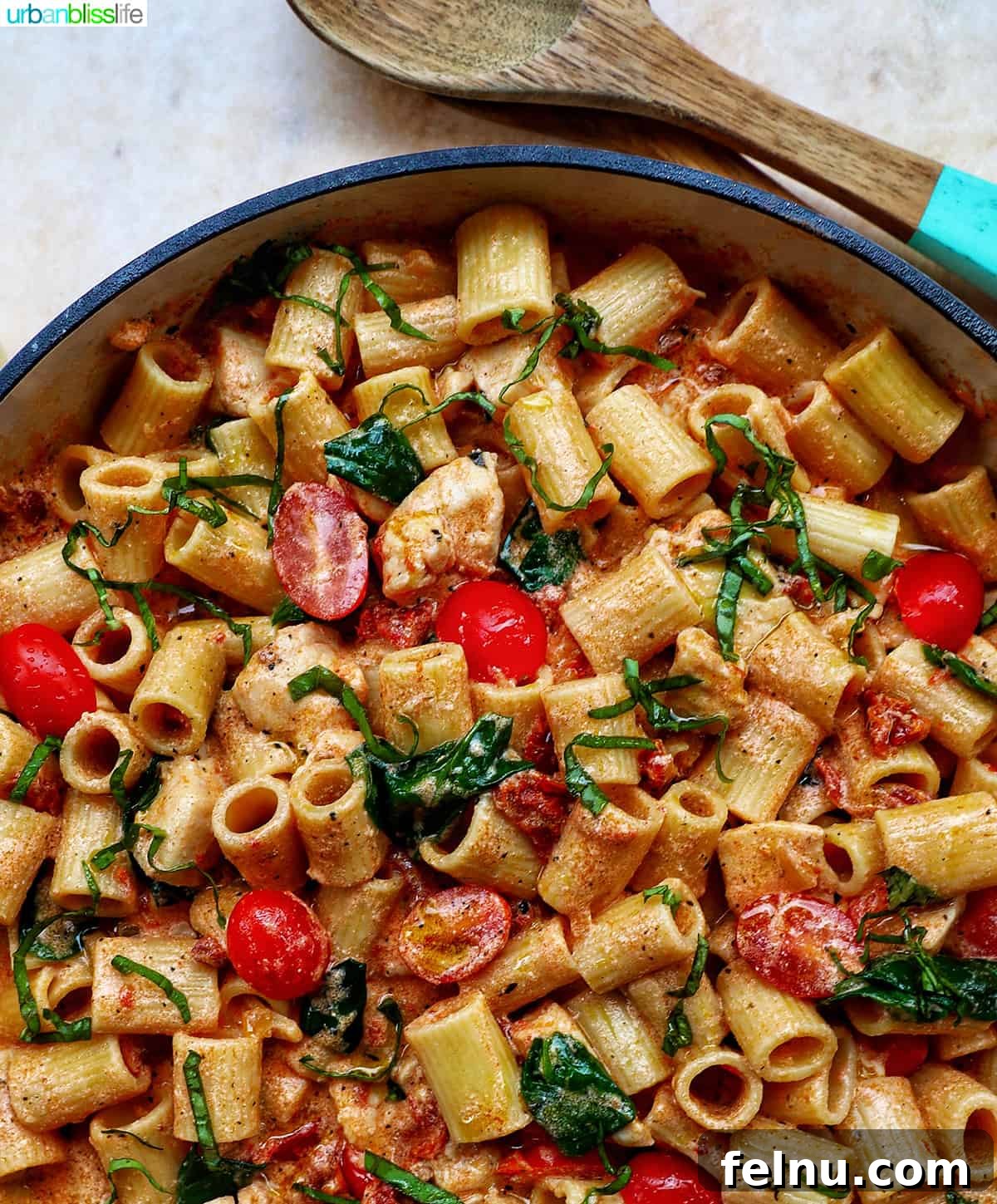 Velvety Tuscan Chicken Pasta 20 A wooden serving spoon resting in a large skillet filled with creamy Tuscan chicken pasta, ready to be served.