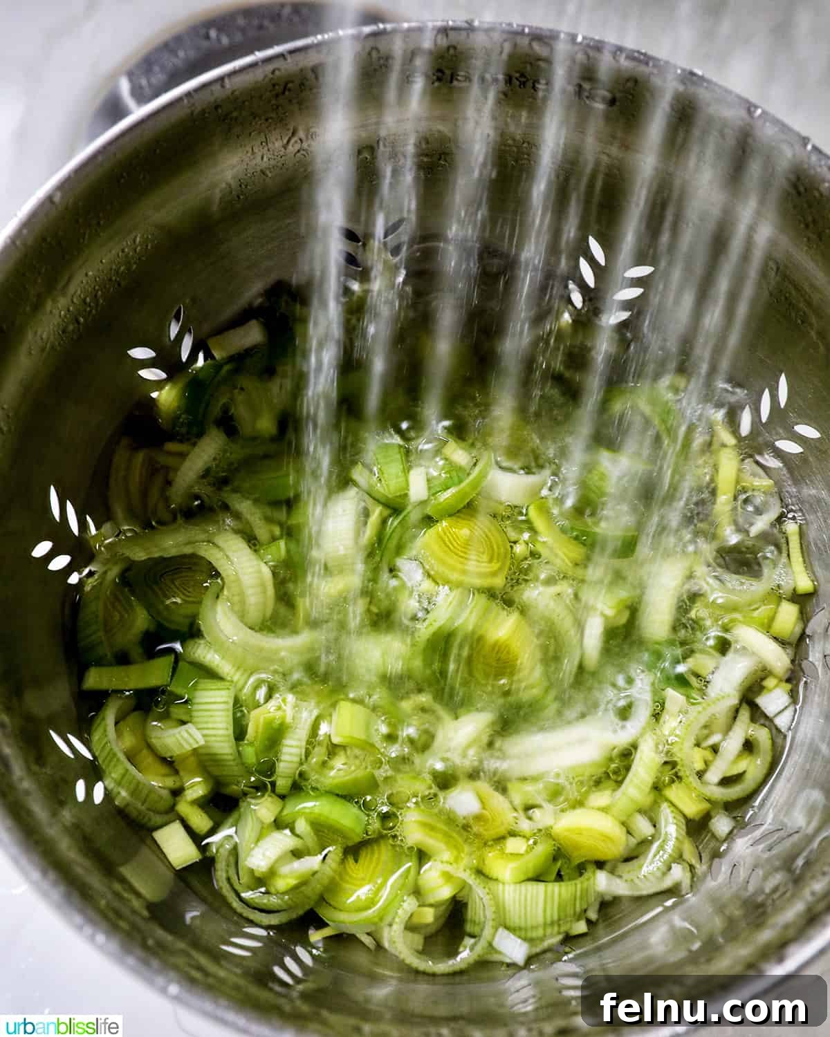 Smoked Salmon & Dill Quiche 19 Close-up of water rinsing thinly sliced leeks in a colander in a kitchen sink, illustrating the cleaning process.