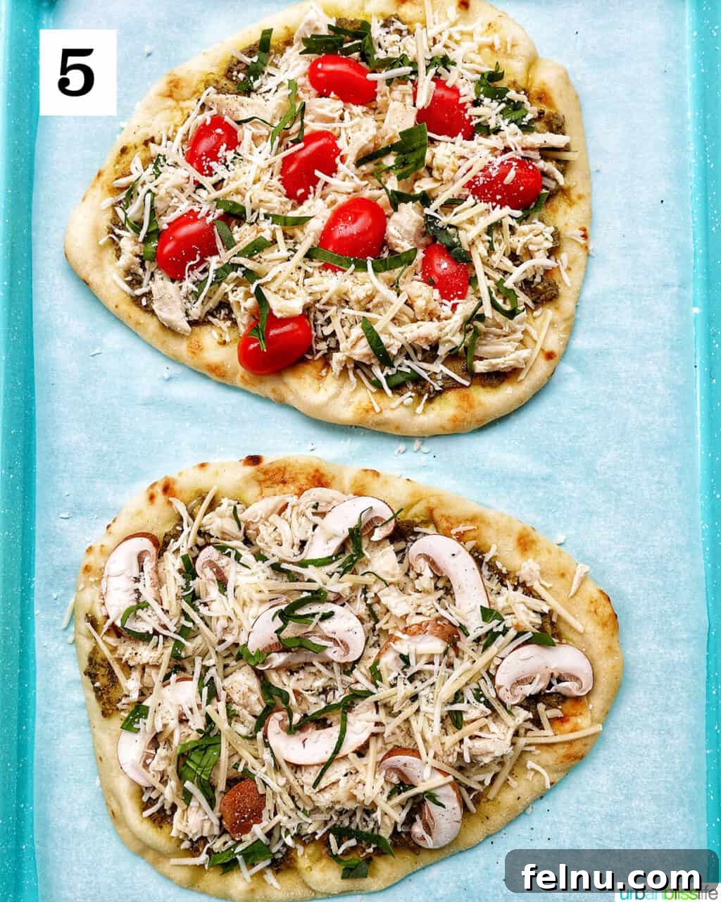 Two chicken pesto flatbreads, one with tomatoes and one with mushrooms, topped with the final layer of cheese.