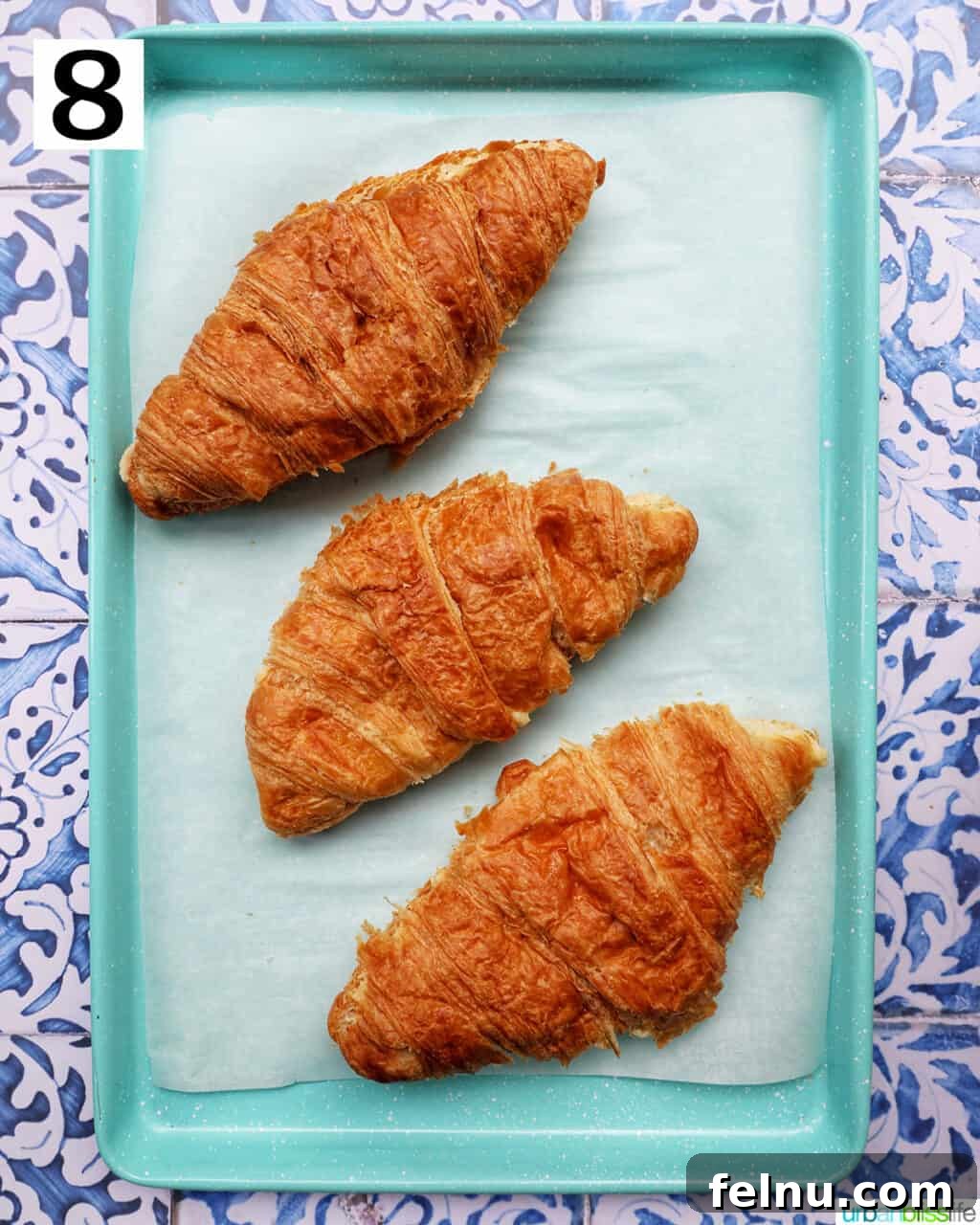Three almond croissants placed on a prepared baking sheet, ready to be baked.