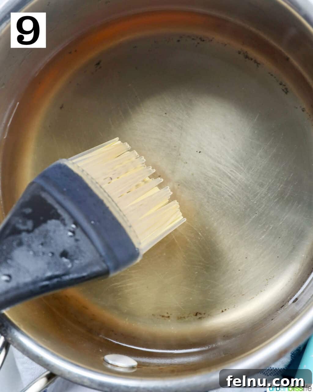 A pastry brush dipped in almond syrup in a saucepan.