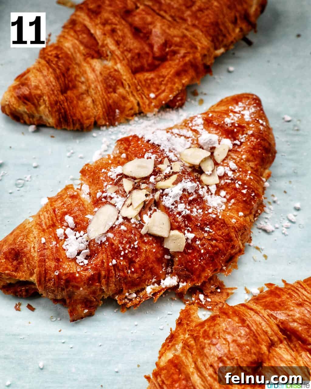 Three almond croissants on a baking sheet, brushed with syrup and ready for toppings.