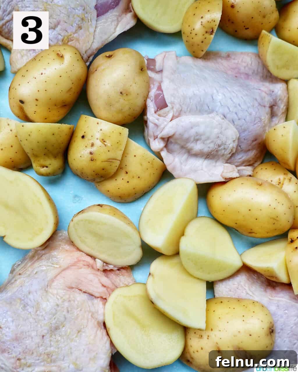 Tek Tepside Tavuklu Patates 8 raw chicken and baby potatoes on a sheet pan.