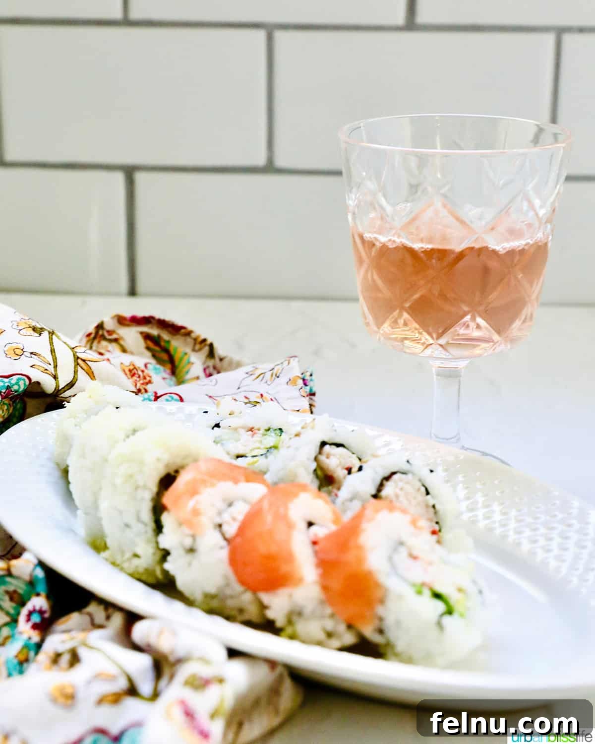Glass of rosé wine with a plate of sushi rolls.