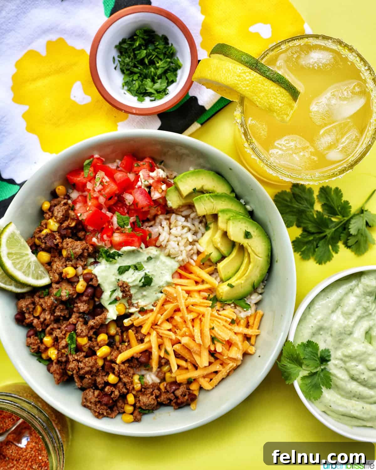 Effortless Fiesta Bowls 15 Taco bowl with ground beef, beans, cheese, pico de gallo, avocado, rice, avocado cilantro lime crema, alongside a yuzu margarita.