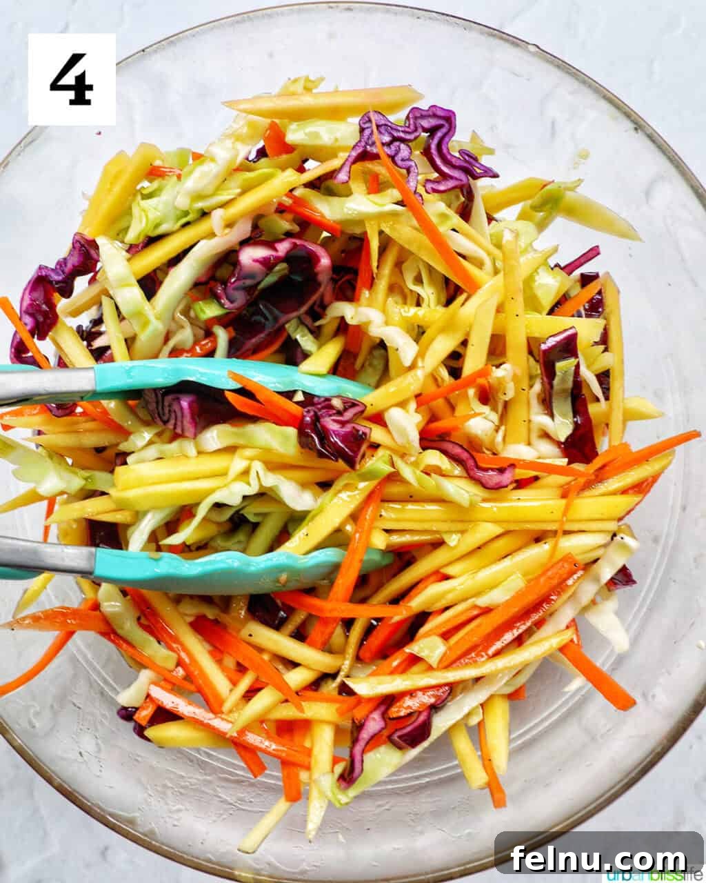 Mango Coleslaw 8 Mango slaw with fresh herbs and kitchen tongs in a bowl.