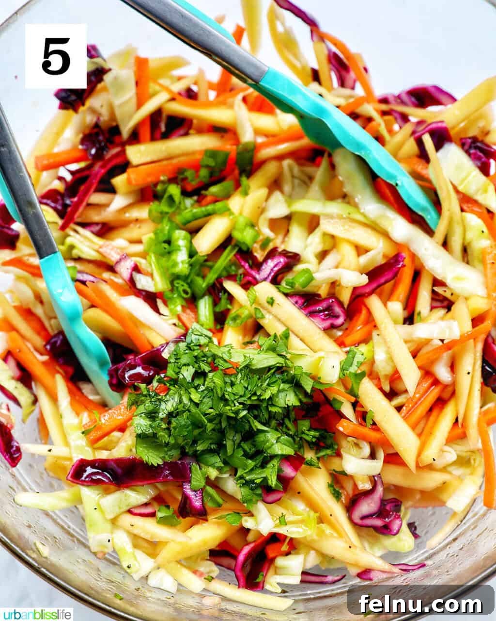 Mango Coleslaw 9 Mango slaw with fresh herbs and kitchen tongs in a bowl.