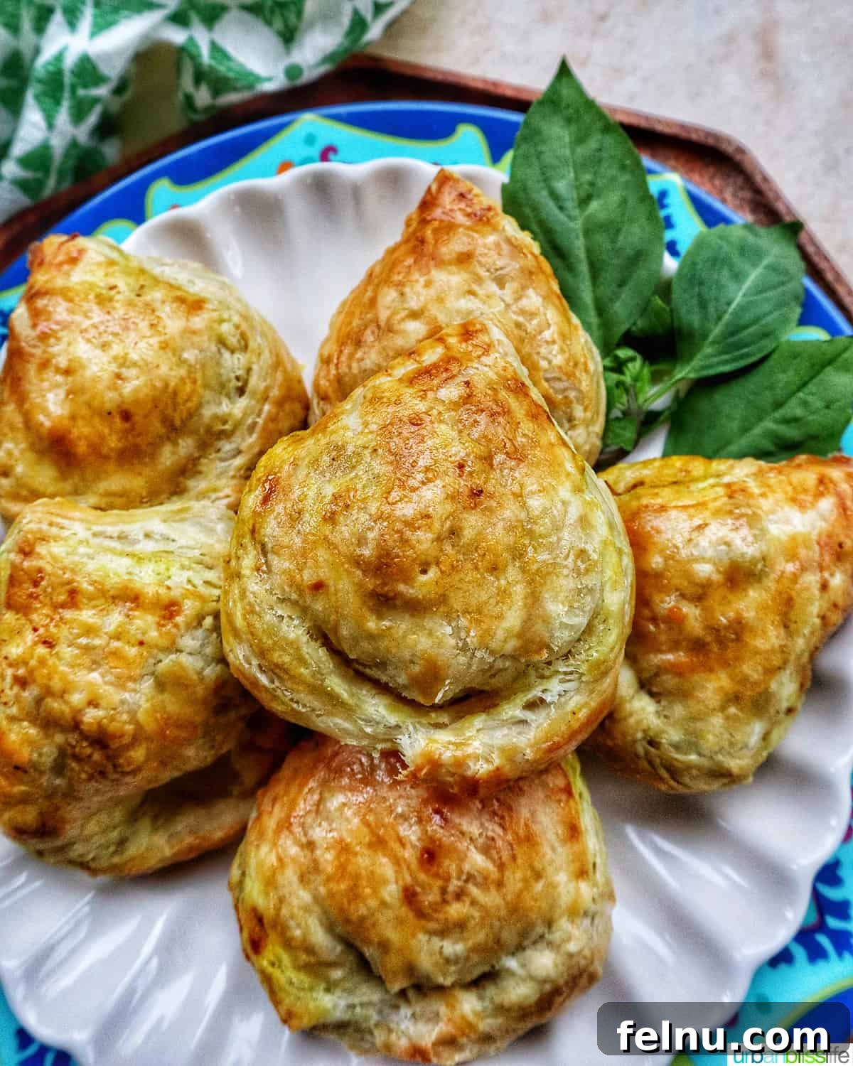 Must-Try Thai Dishes 9 several baked Thai curry puff appetizers on a plate with side of Thai basil.
