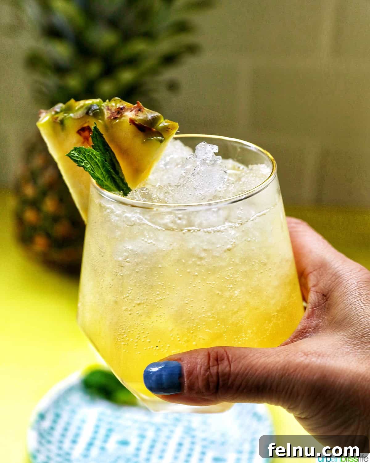 A hand holding a glass of Pineapple Mocktail, showcasing its refreshing appearance.