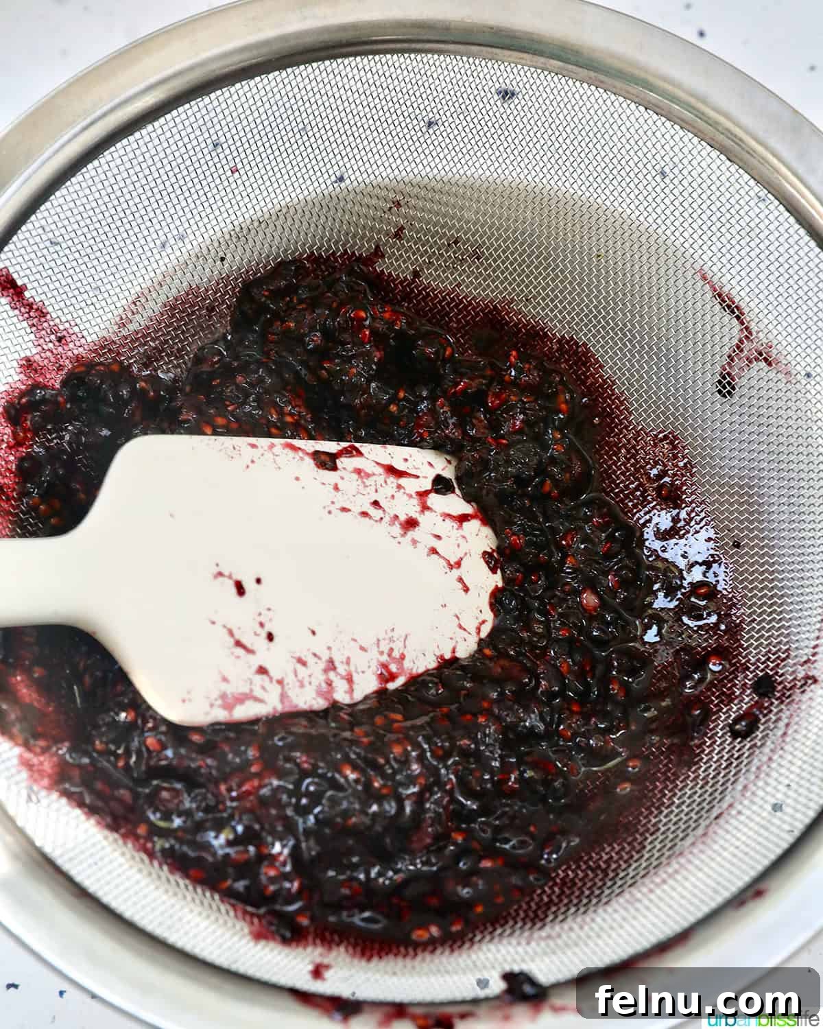 Homemade No-Cook Blackberry Jam 17 spatula straining blackberry freezer jam through a sieve.