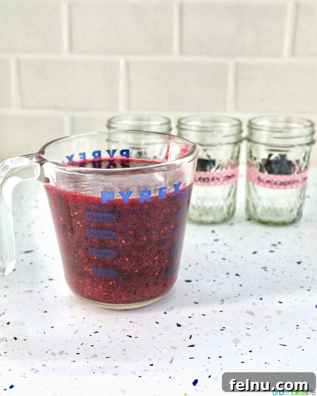 Homemade No-Cook Blackberry Jam 19 blackberry freezer jam in a large measuring cup next to empty mason jars.