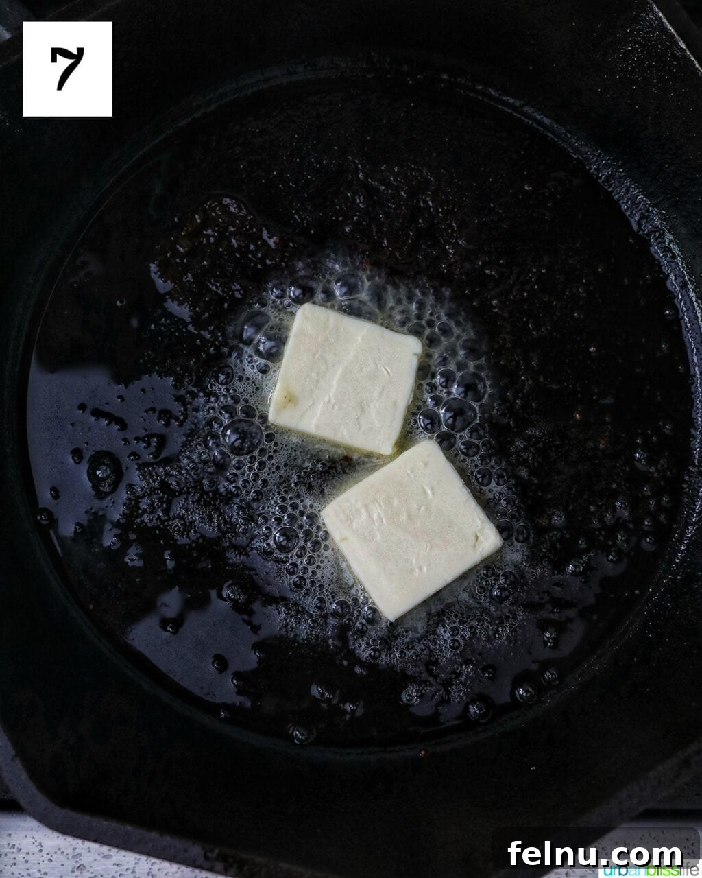 Two pats of butter melting in a cast iron skillet.
