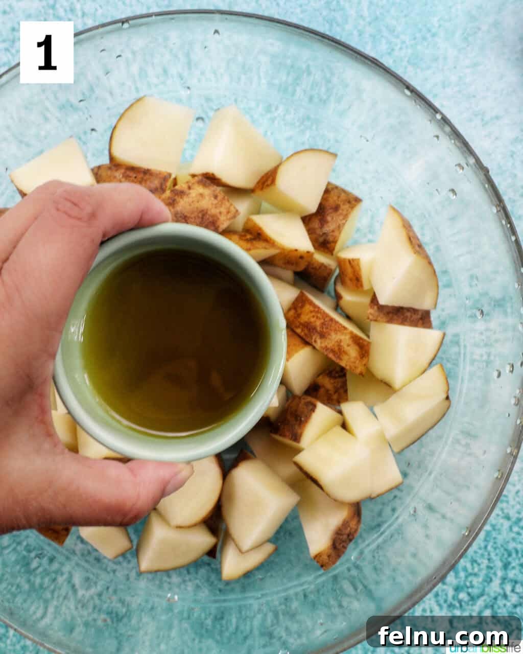Crispy Rosemary Garlic Potatoes 5 hand holding bowl of olive oil over a glass bowl with potato wedges.