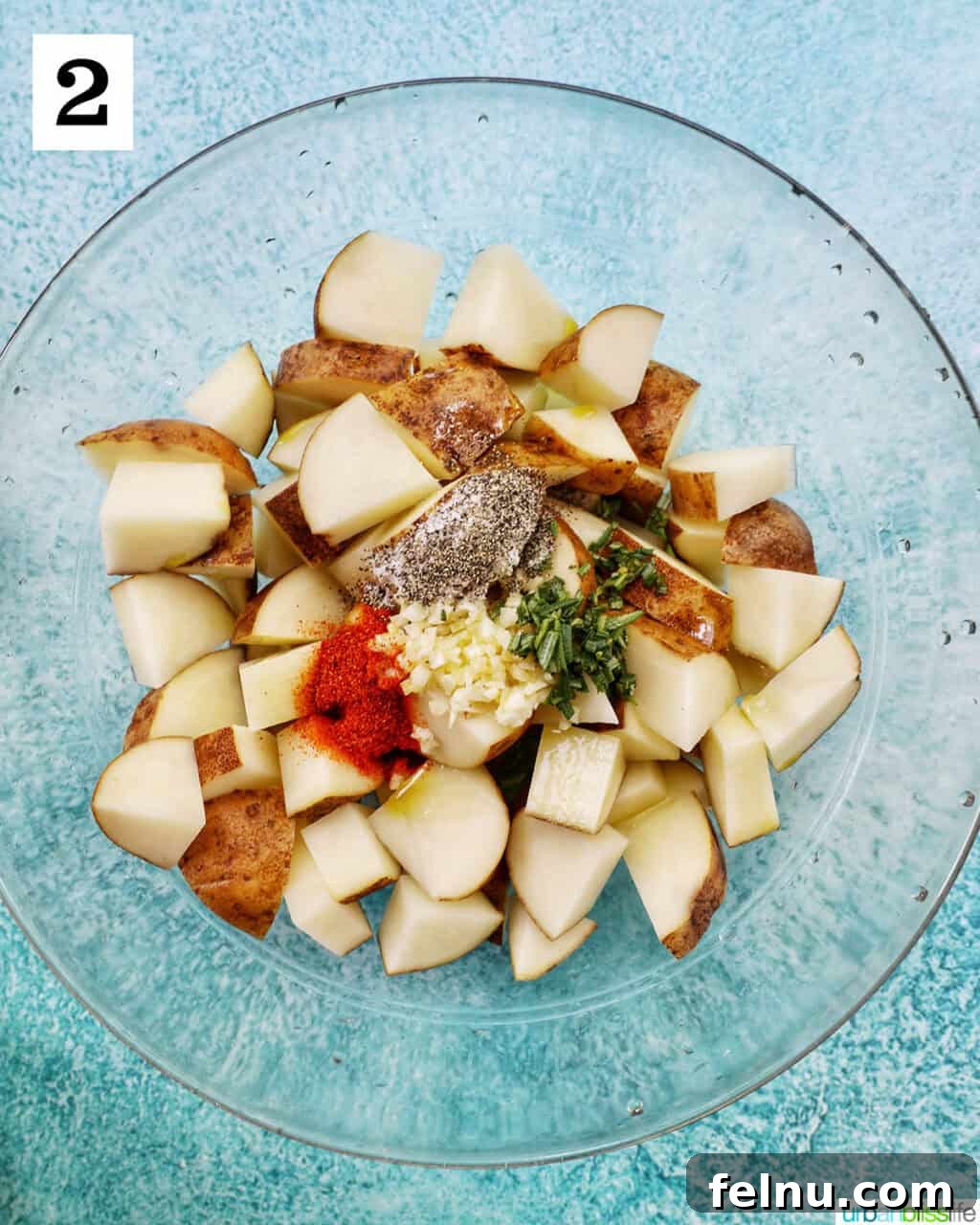 Crispy Rosemary Garlic Potatoes 6 glass bowl with potato wedges, seasonings, and herbs.