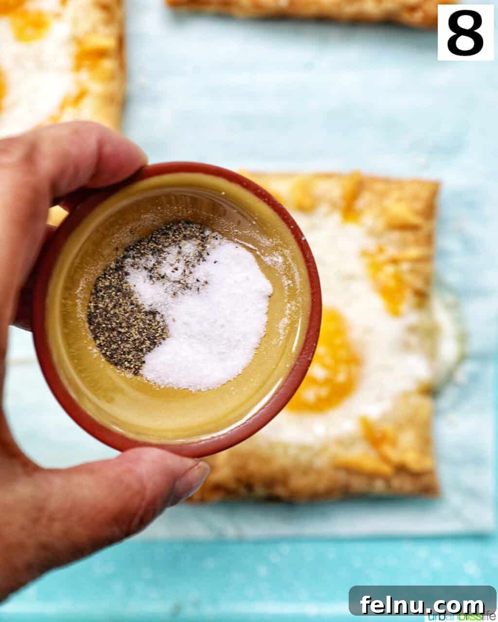 Golden Egg Parcels 14 A hand seasoning eggs in puff pastry with salt and pepper from a small bowl.