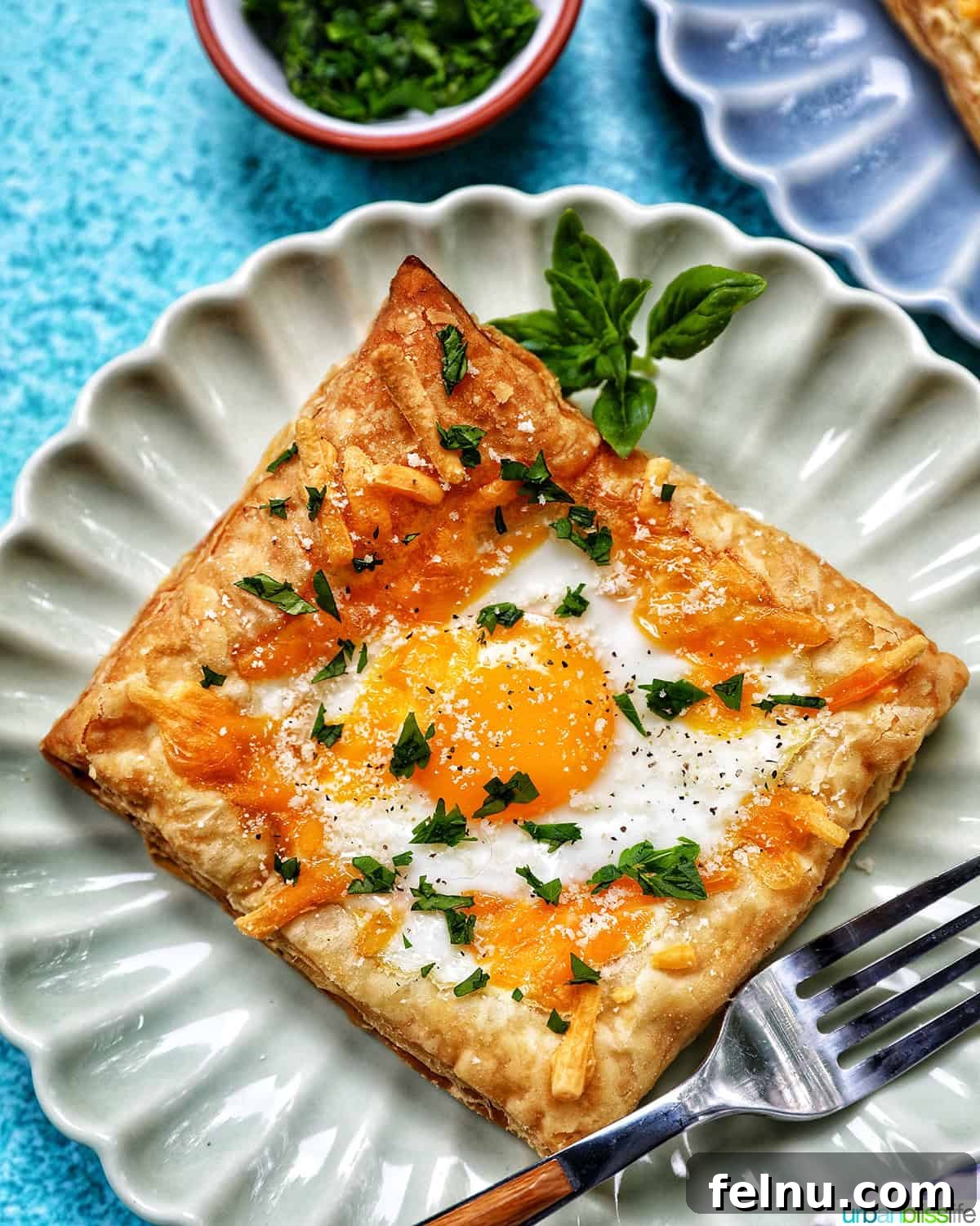 Golden Egg Parcels 16 Overhead shot of an egg in puff pastry on a plate with fresh parsley garnish.