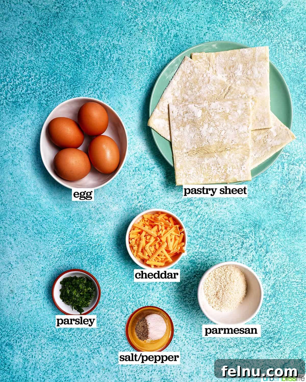 Golden Egg Parcels 4 Bowls and plates displaying ingredients for eggs in puff pastry, including pastry dough, cheese, eggs, and herbs.