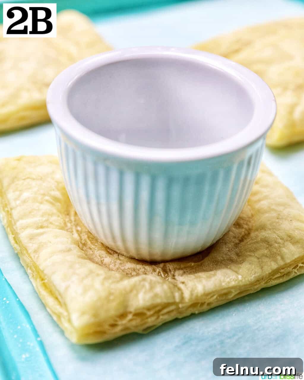 Golden Egg Parcels 7 Another view of a white ramekin on a puff pastry square, illustrating how to press down to form a well.