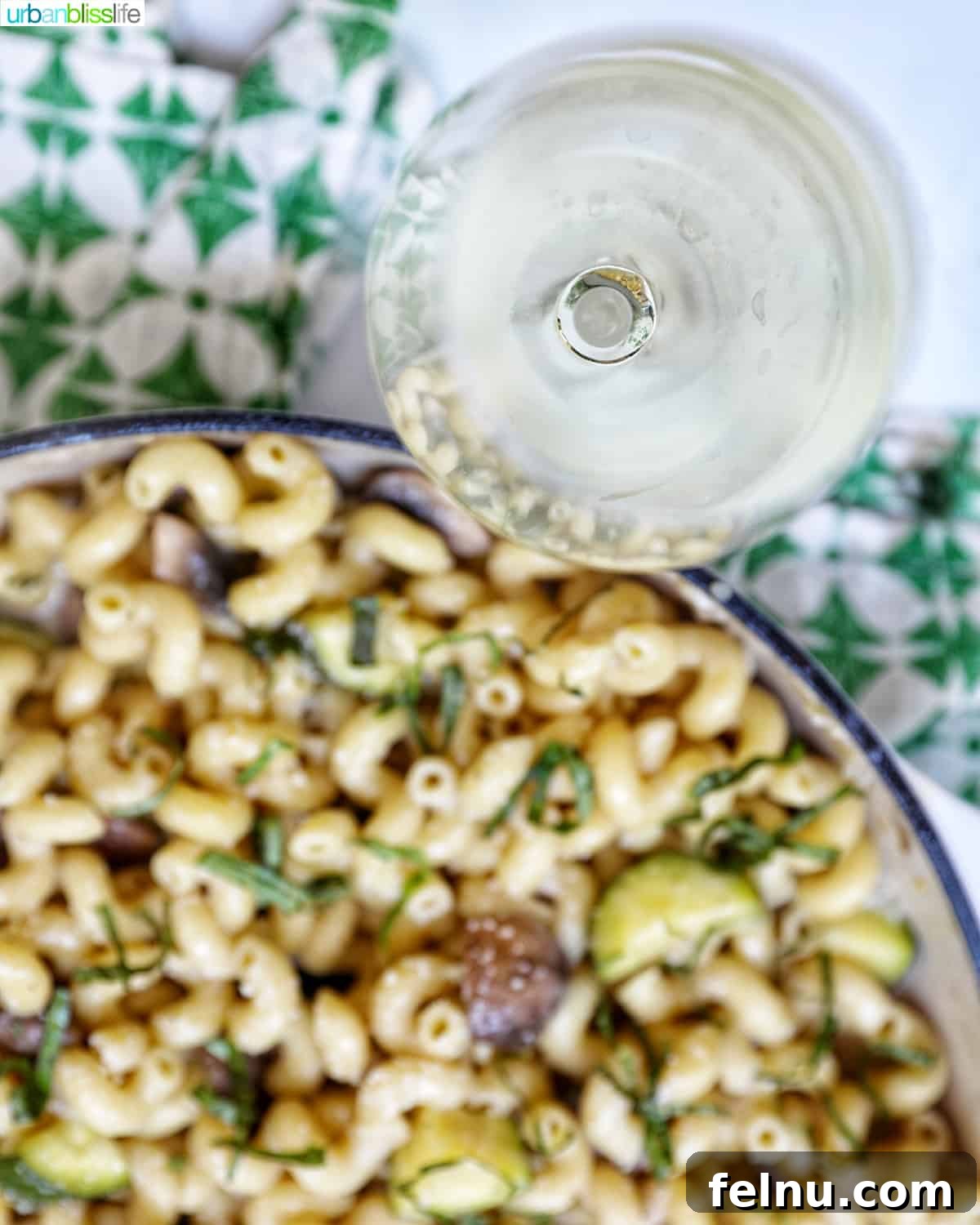 Savory Mushroom Toasts 21 Overhead photo of a glass of white wine placed next to a pan of pasta, adorned with a green and white napkin.