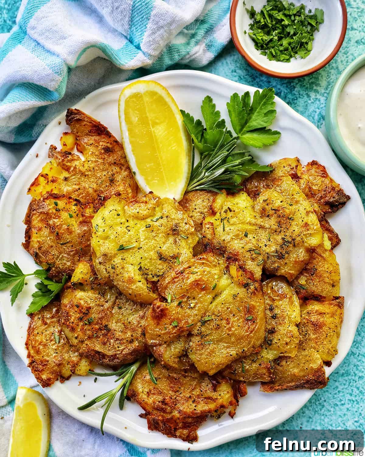 Crispy Air-Fried Smashed Potatoes 2 Crispy smashed potatoes on a plate with fresh herbs and lemon wedges, viewed from overhead.