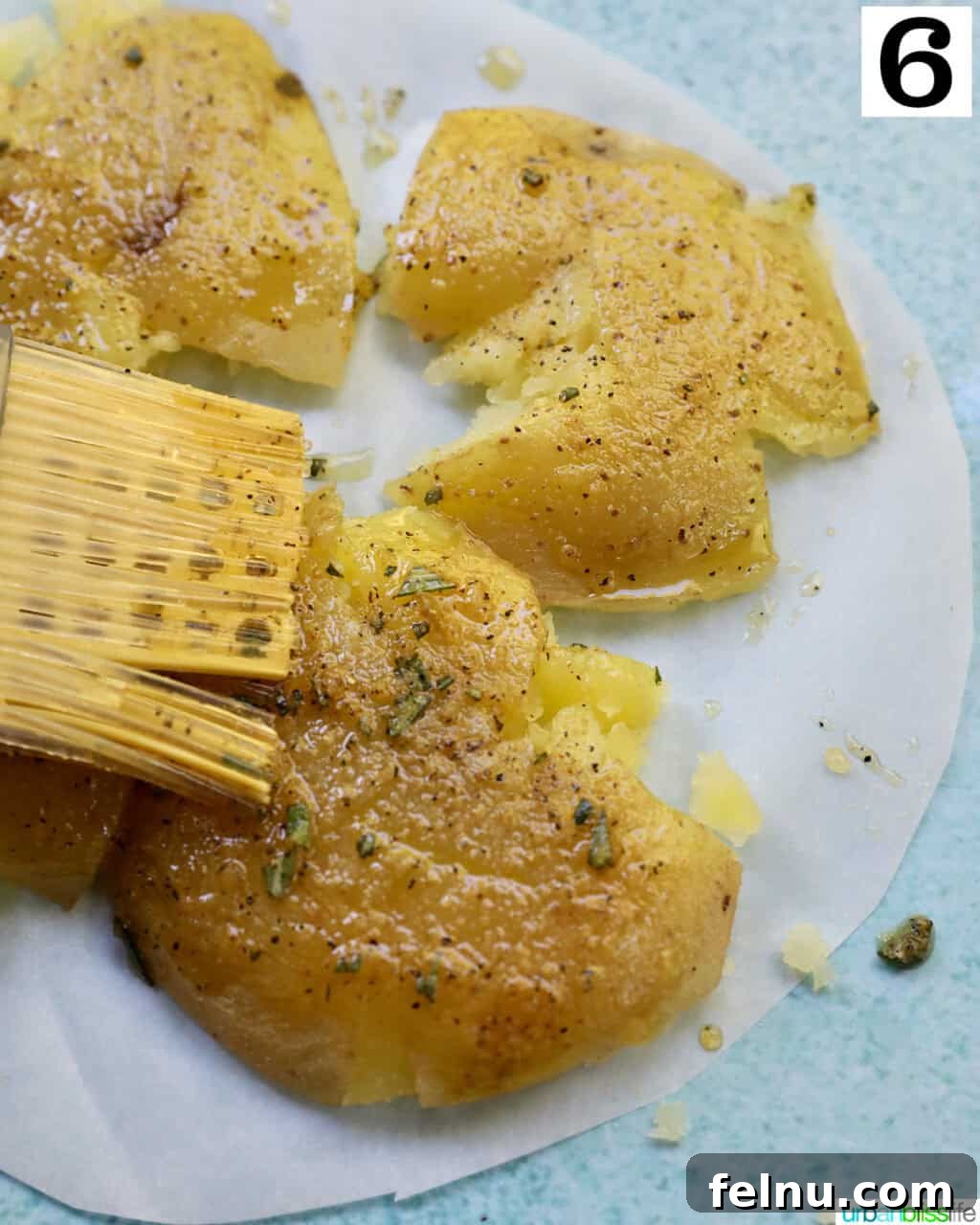 Crispy Air-Fried Smashed Potatoes 12 A pastry brush applying the olive oil herb mixture onto smashed potatoes arranged on a cutting board.