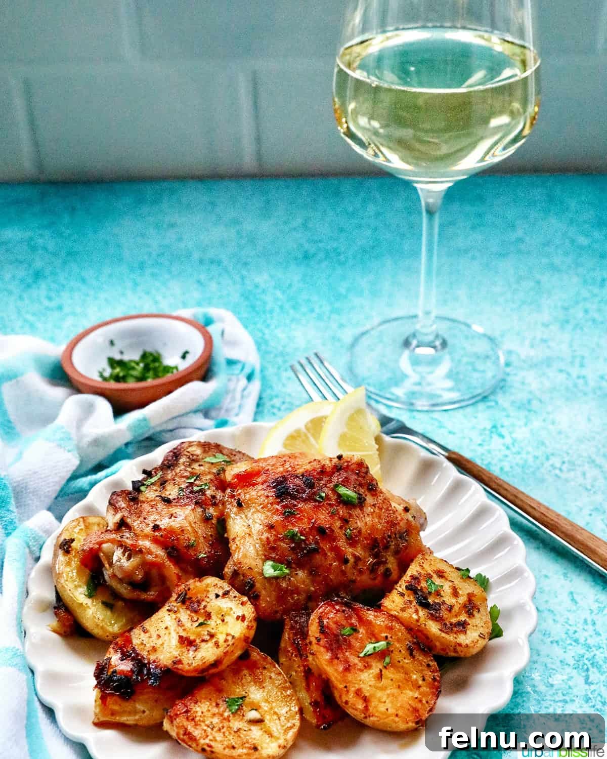 Crispy Air-Fried Smashed Potatoes 18 A plate featuring chicken and smashed potatoes, alongside a fork, a glass of white wine, and a small bowl of chopped parsley.