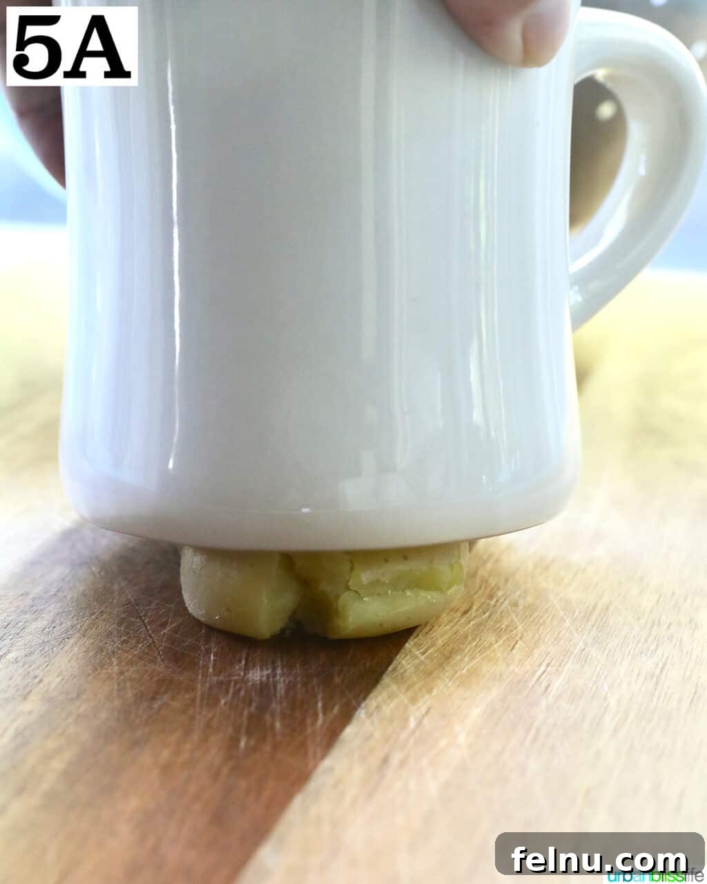 Crispy Air-Fried Smashed Potatoes 10 A white mug gently pressing down on a single baby potato on a cutting board, smashing it flat.