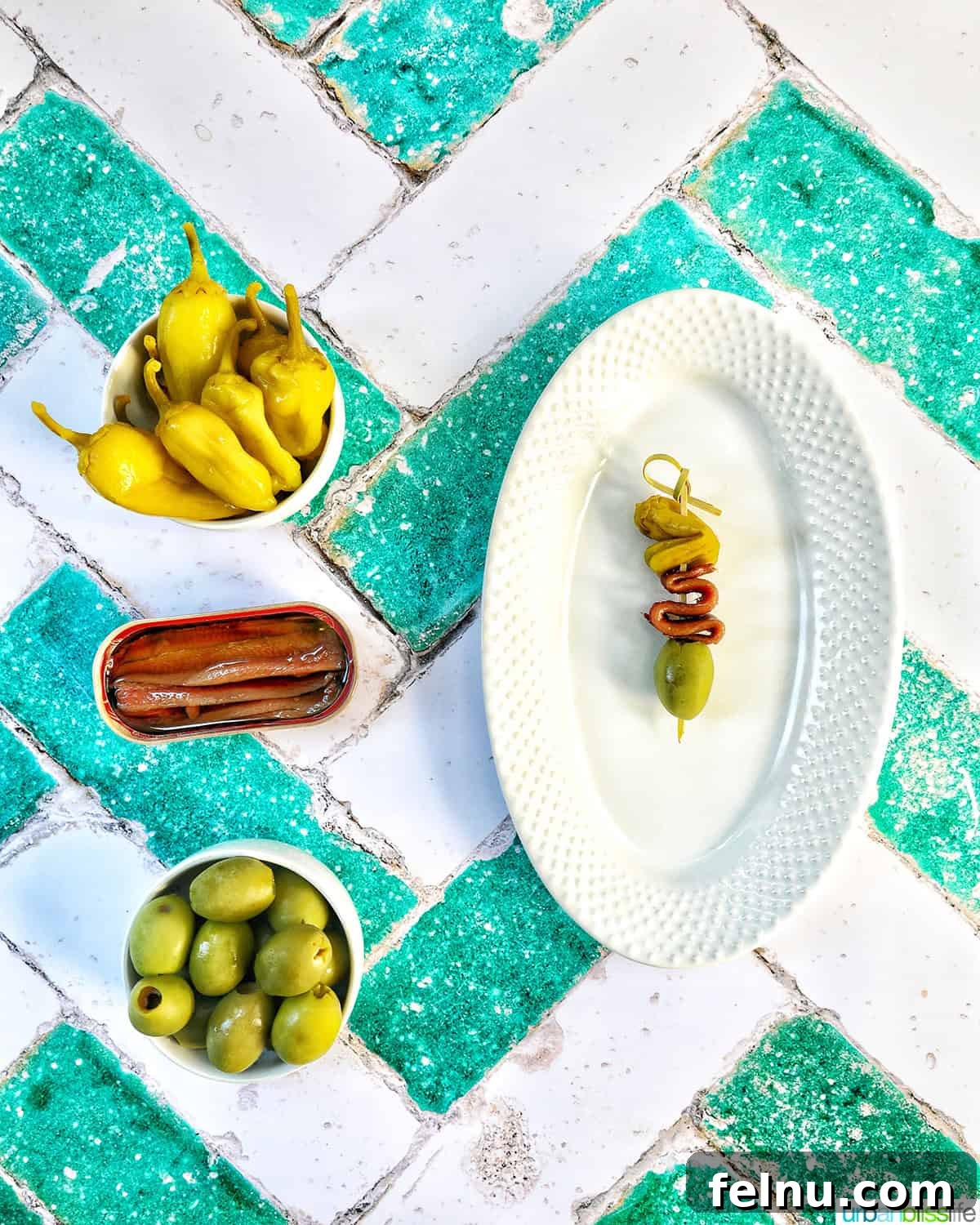 Gilda A Basque Classic 12 Bowls of peppers, anchovies, and olives arranged next to a plate featuring a single Gilda pintxo, highlighting the simplicity of ingredients.