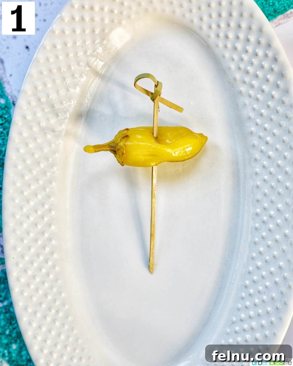 Gilda A Basque Classic 5 White plate with a single food pick with a pickled pepper, the first step in assembling a Gilda pintxo.