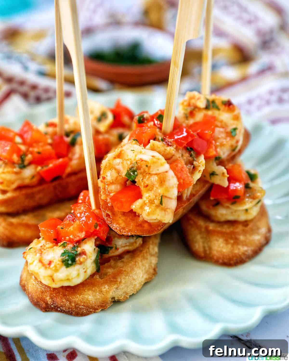 Savory Shrimp Bites 2 shrimp pintxos skewers with tomatoes on crostini bread on a scalloped plate.