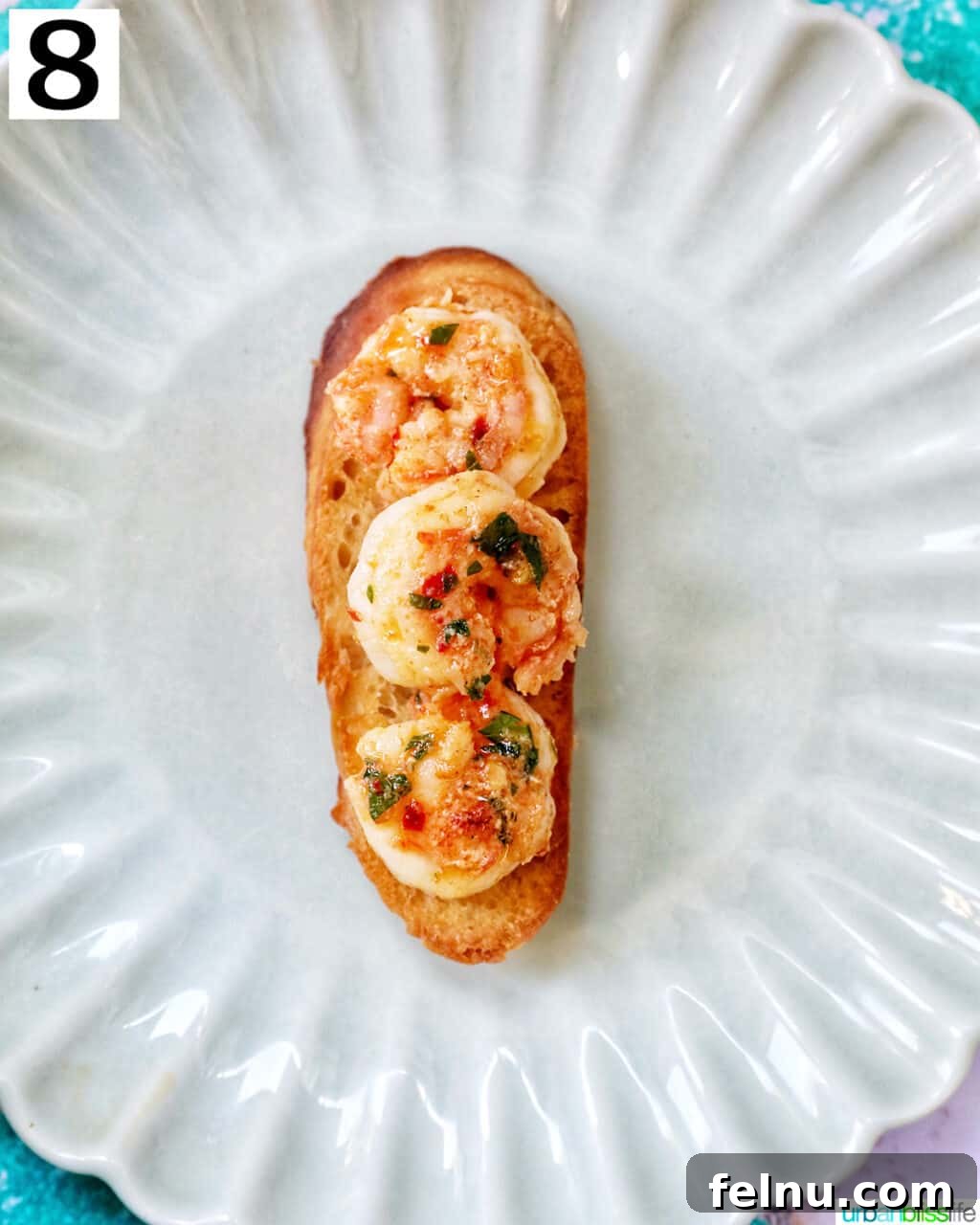 Savory Shrimp Bites 13 shrimp on sliced baguette bread on a scalloped plate.