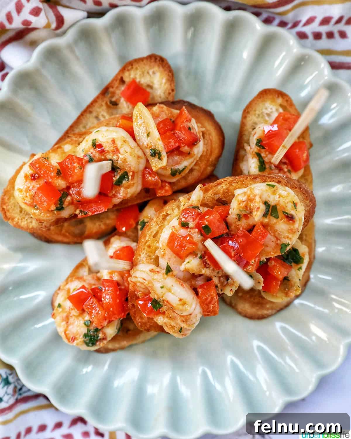 Savory Shrimp Bites 15 shrimp pintxos skewers with tomatoes on crostini bread on a scalloped plate.