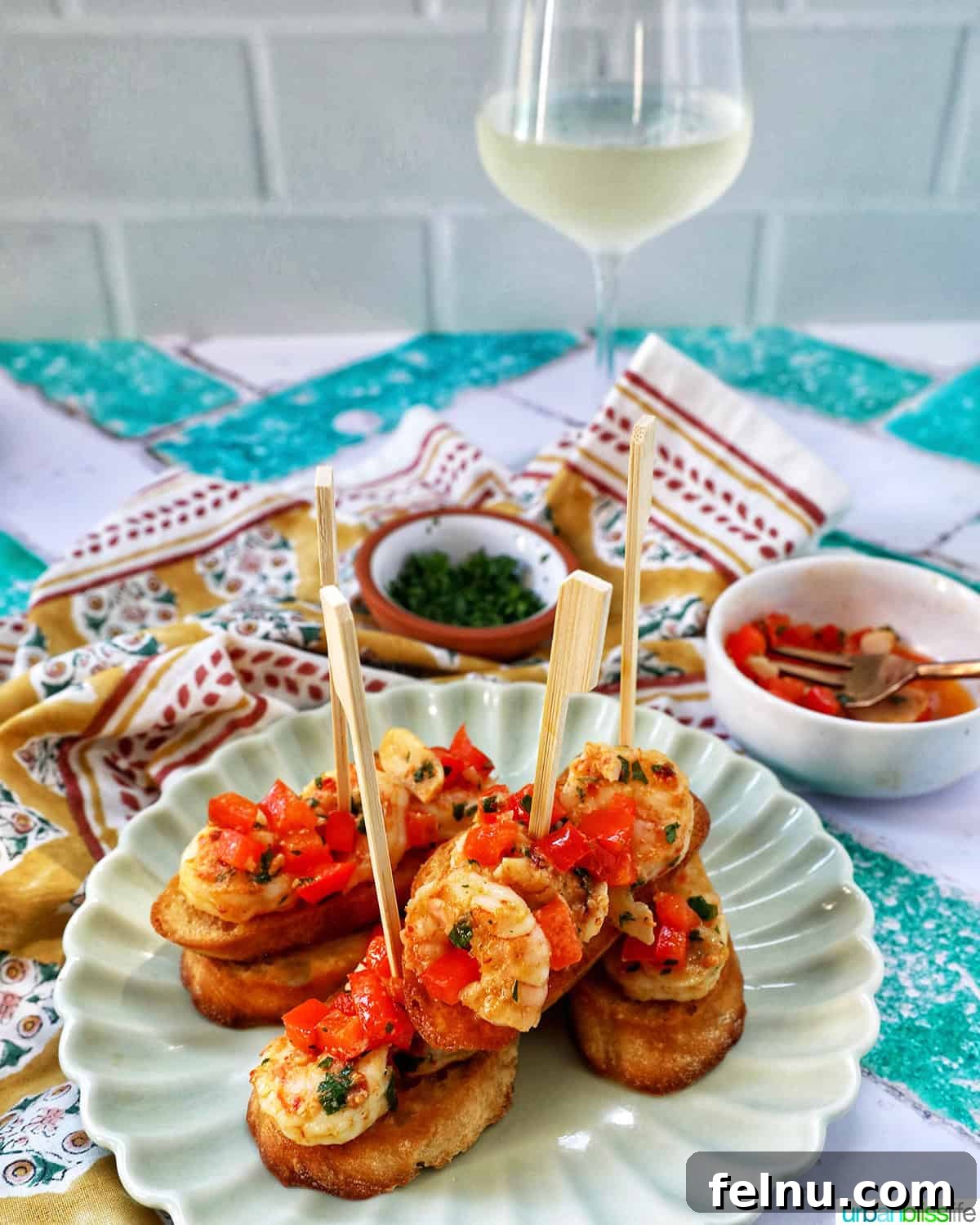 Savory Shrimp Bites 17 shrimp pintxos skewers with tomatoes on crostini bread on a scalloped plate with a glass of white wine.