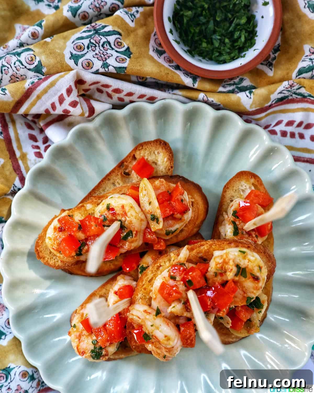 Savory Shrimp Bites 3 shrimp pintxos skewers with tomatoes on crostini bread on a scalloped plate.