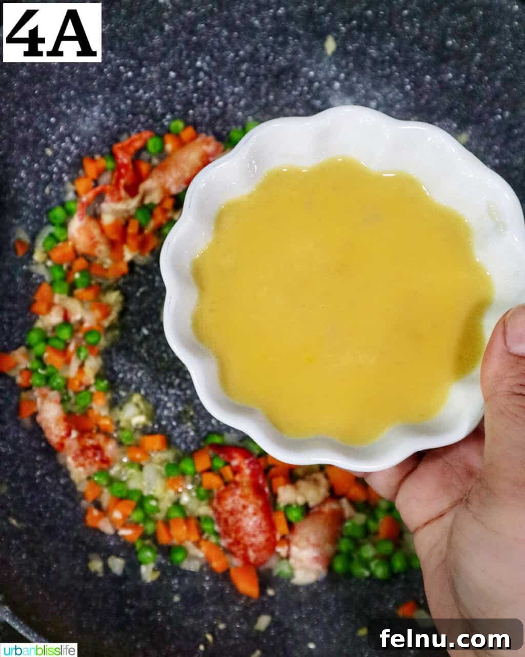 Decadent Lobster Fried Rice 10 hand holding a bowl of beaten eggs over a wok with fried rice.