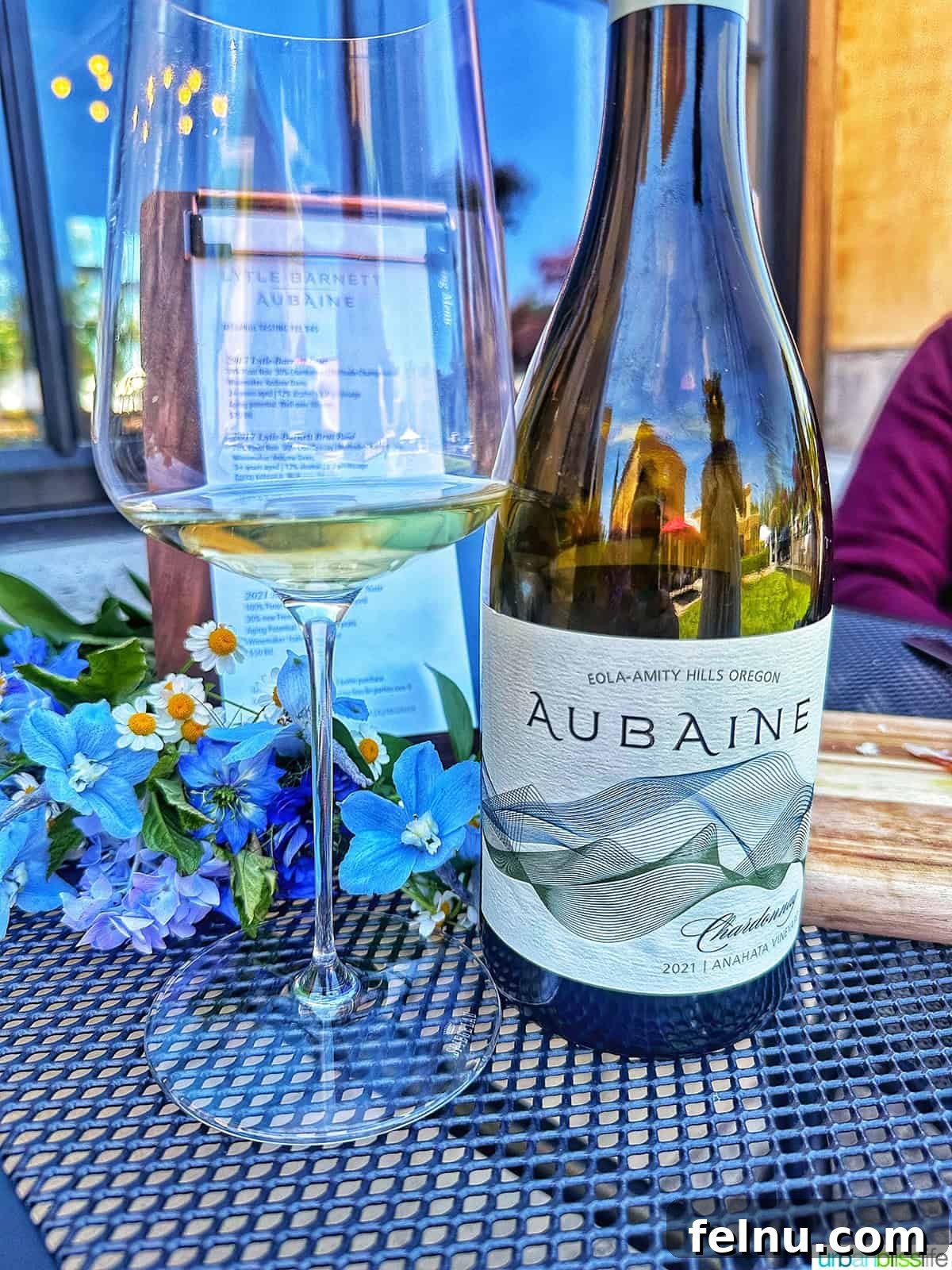 Lytle-Barnett & Aubaine Vintners Lounge 6 A glass of Aubaine Wines Chardonnay next to its elegant bottle, showcasing the wine's golden hue.