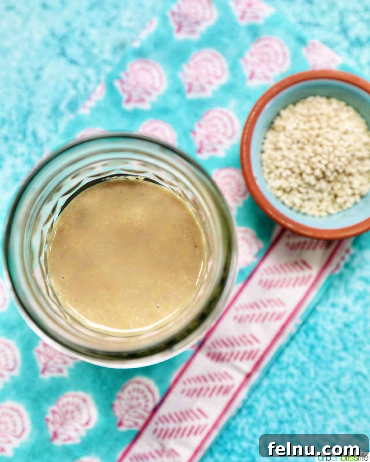 Crafting Your Own Tahini 2 jar of homemade tahini with a small bowl of sesame seeds and a spoon.