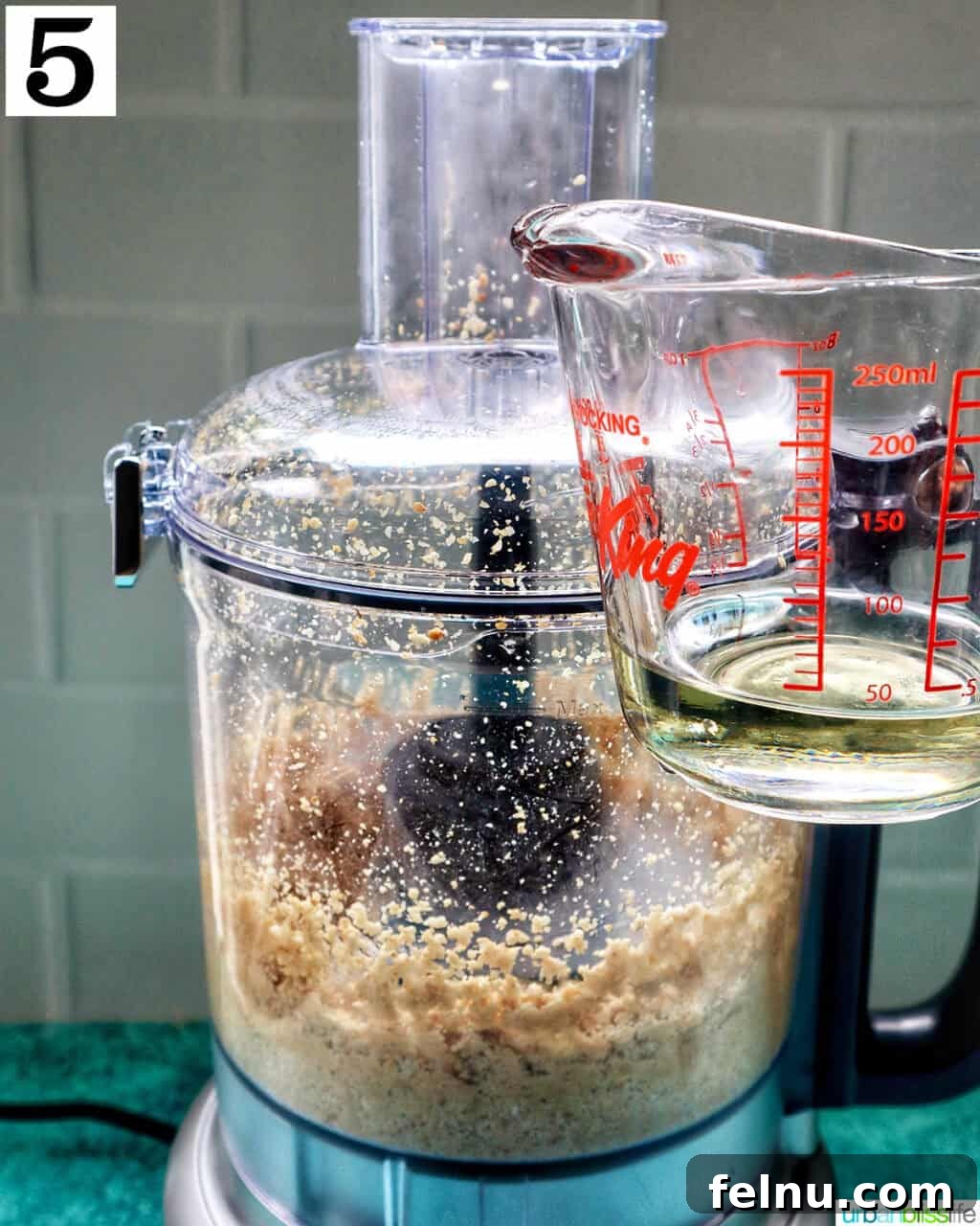 Crafting Your Own Tahini 11 measuring cup with oil next to a food processor with tahini.