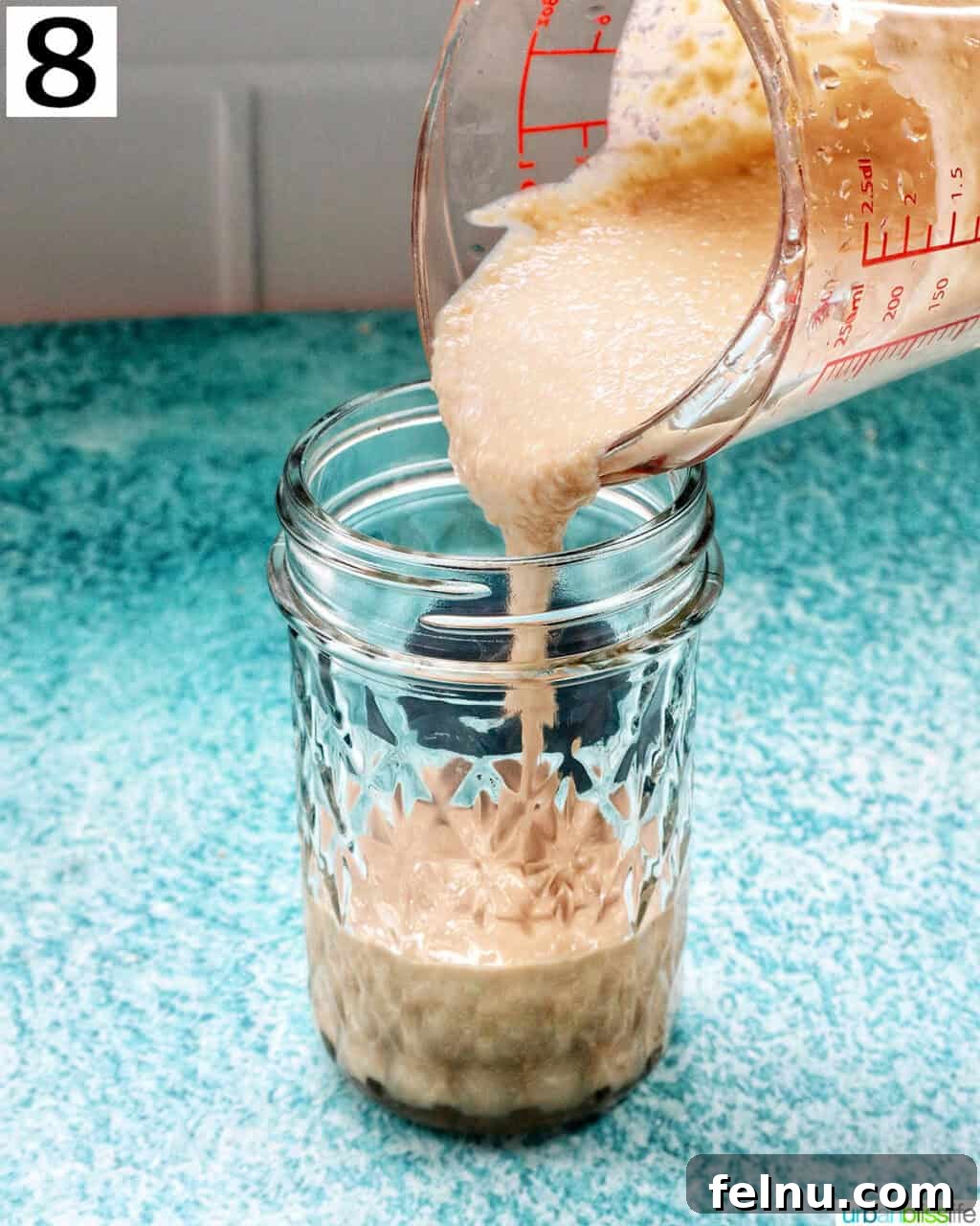 Crafting Your Own Tahini 14 pouring homemade tahini into a mason jar.