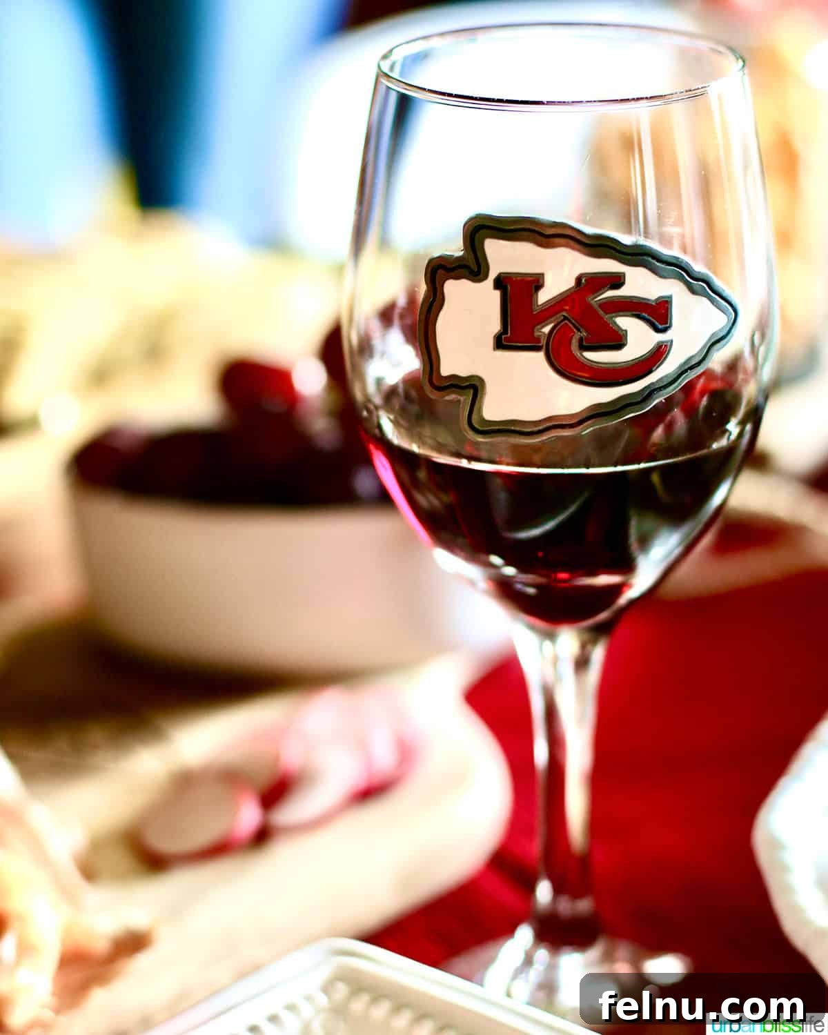 Ultimate Game Grub 7 A wine glass with 'KC' logo, set against a backdrop of a football game, suggesting a sophisticated touch to tailgating.