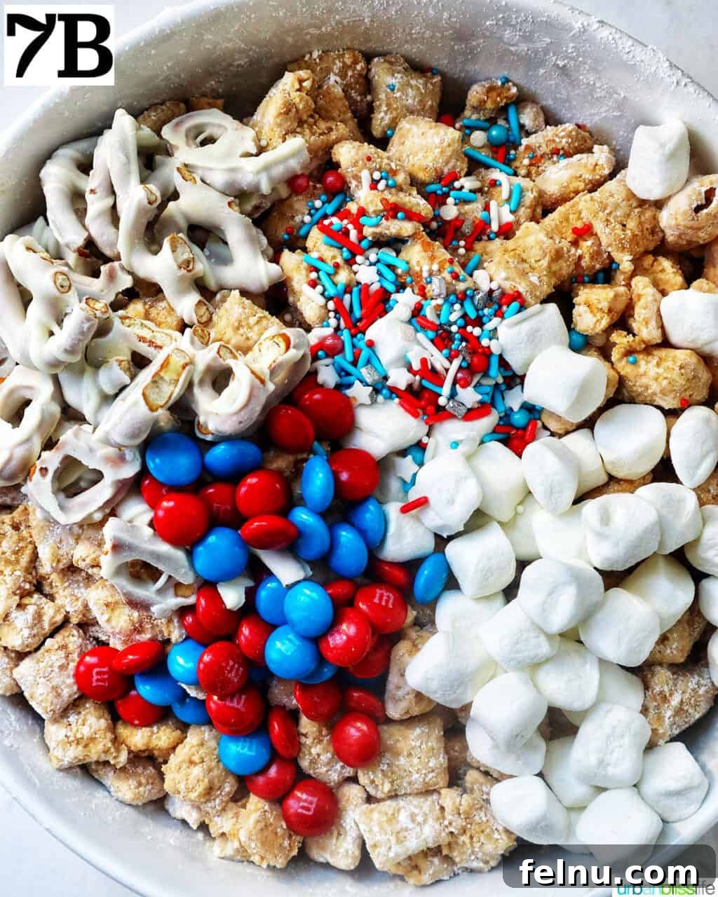 Effortlessly Delicious Patriotic Puppy Chow 14 Large bowl filled with patriotic puppy chow, marshmallows, red and blue M&M candies, and pretzels, ready to be mixed.