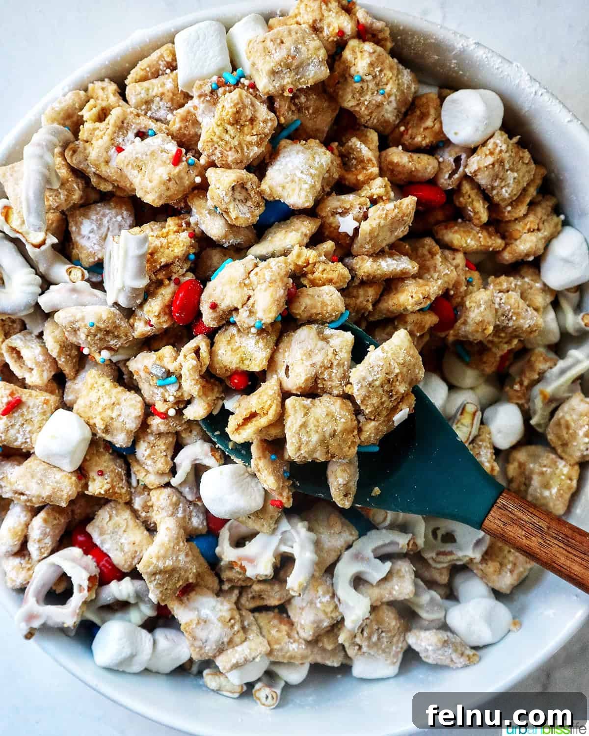 Effortlessly Delicious Patriotic Puppy Chow 18 A serving spoon dipped into a large bowl of patriotic puppy chow.