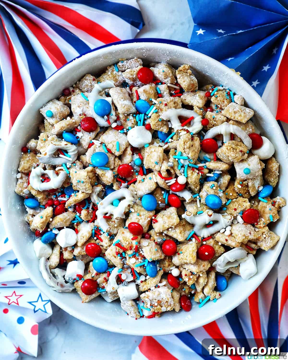 Effortlessly Delicious Patriotic Puppy Chow 3 Overhead view of a large bowl of patriotic puppy chow, surrounded by red, white, and blue decorations like small flags and star confetti.