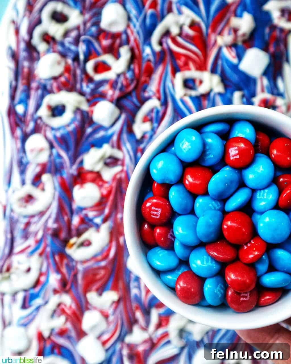 Fourth of July Freedom Bark 13 A hand holding a bowl of colorful red and blue M&Ms, sprinkling them generously over the wet red, white, and blue chocolate bark.