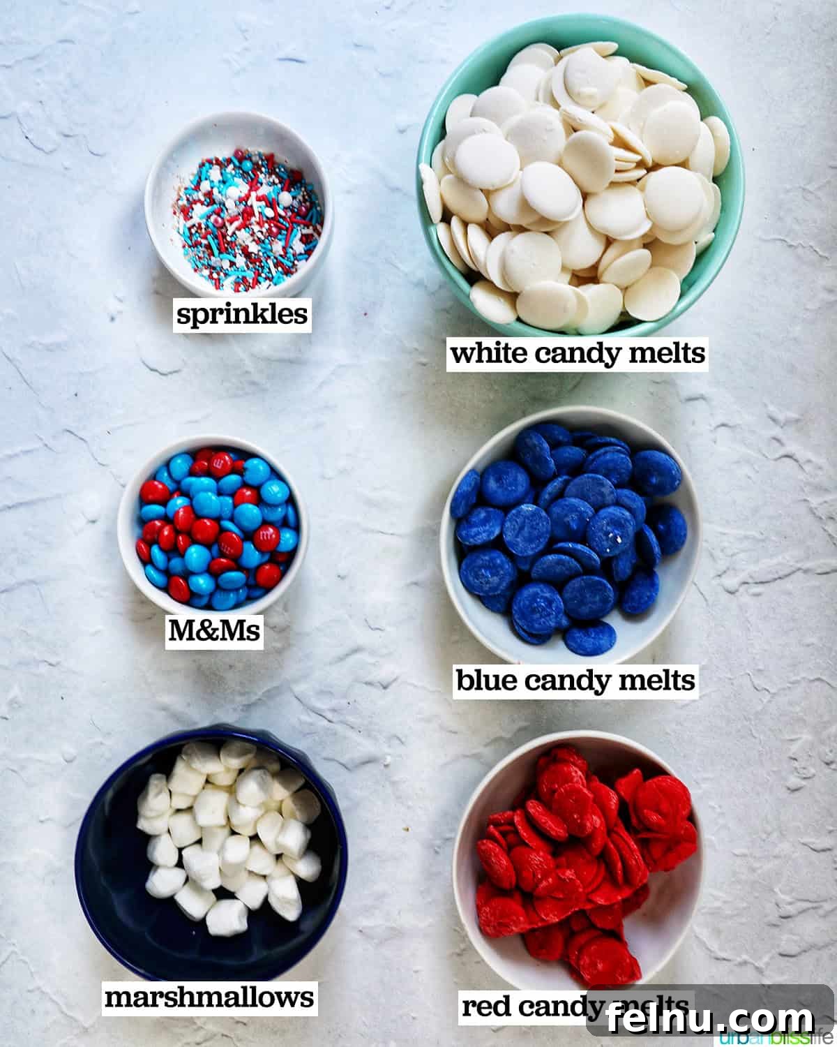 Fourth of July Freedom Bark 4 bowls of ingredients, including white chocolate chips, red candy melts, blue candy melts, and assorted toppings, ready to make patriotic bark.