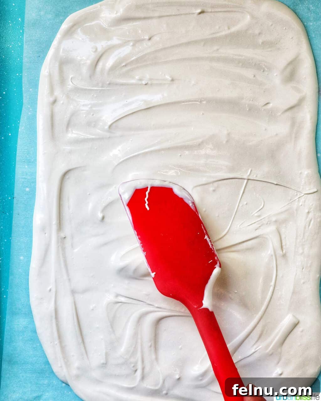 Fourth of July Freedom Bark 5 A red spatula gracefully spreading melted white chocolate onto a parchment-lined baking sheet, creating a smooth, even base for the bark.