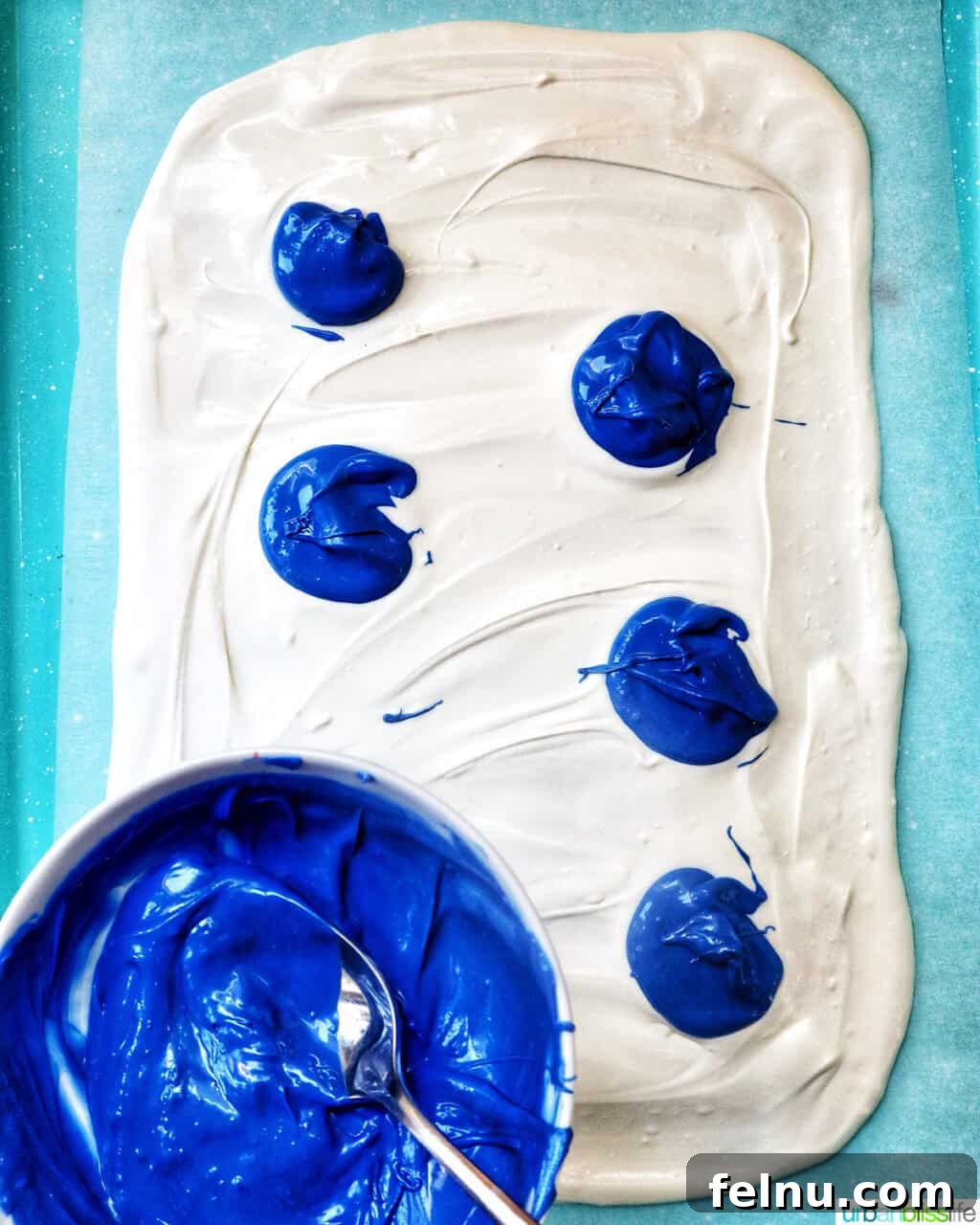 Fourth of July Freedom Bark 6 A baking sheet showcasing a freshly spread layer of melted white chocolate, dotted with vibrant blue melted chocolate, setting the stage for more colors.
